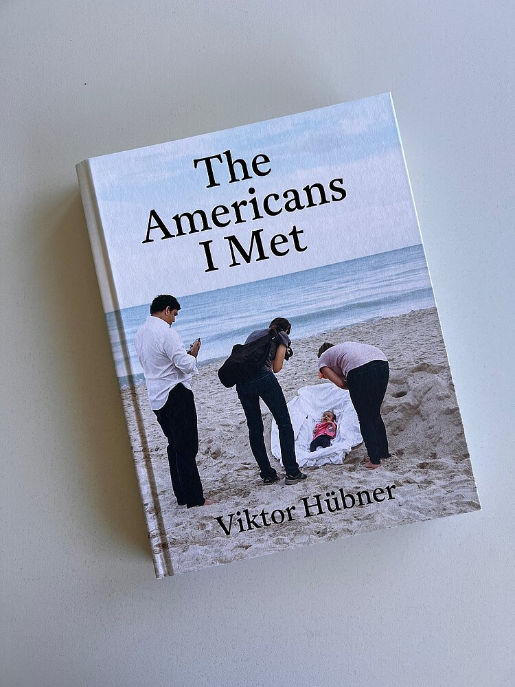 Das Buch „The Americans I Met“ von Viktor Hübner zeigt auf dem Cover eine Szene am Strand mit vier Erwachsenen und einem Baby im weißen Tuch.